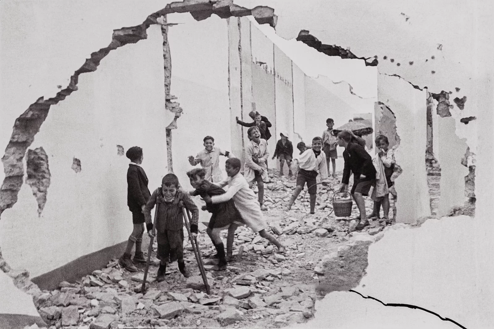 Boys play among rubble inside a roofless structure framed by a jagged opening in a broken wall.
